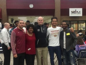 Group photo of diverse smiling people outside brick building with MHM law firm sign, for attorney website.