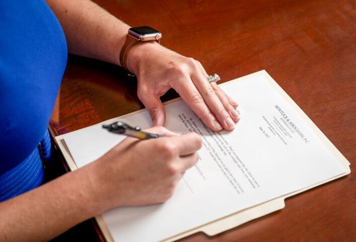 Woman signing legal document on wooden table, close-up of hands with pen and papers, personal injury case