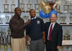 Football player posing with injury attorney, shaking hands in front of trophies to show support