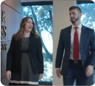 Professional lawyers, a man and woman, walking and smiling in an office setting with large windows.