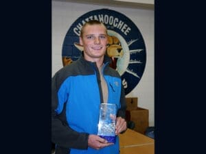 Smiling athlete holding trophy in front of Chattahoochee logo, representing successful recovery from sports injury.