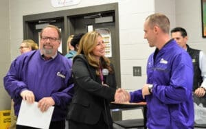 Capstone auto repair shop staff in purple uniforms smiling and conversing with customers at counter