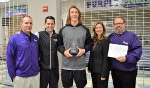 High school athlete receives player of the game award from coaches, trainer, and business owner in gym.