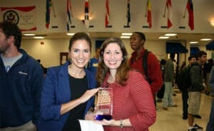 Injury attorney with smiling client holding legal award in office with flags, SEO-friendly alt text