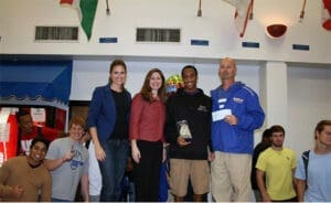 Athletic coach and team posing with award in school gym after championship victory