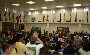 Crowded school cafeteria with diverse students, flags of various countries decorating the walls