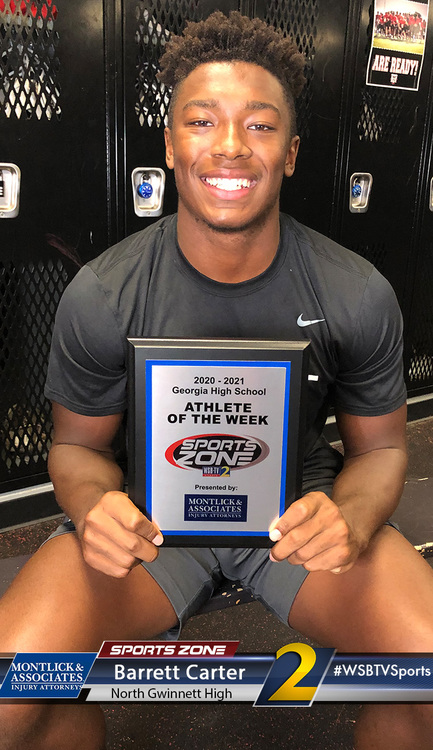 Smiling high school athlete of the week holding Sports Zone award sign in locker room, promoting local business.