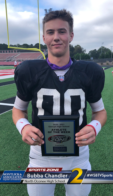 Alt text: High school football player holding Athlete of the Week award on football field