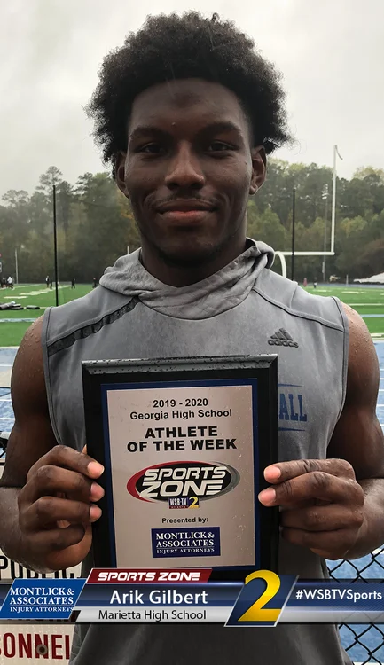 Marietta High School athlete holding Athlete of the Week award on a football field, smiling at camera.