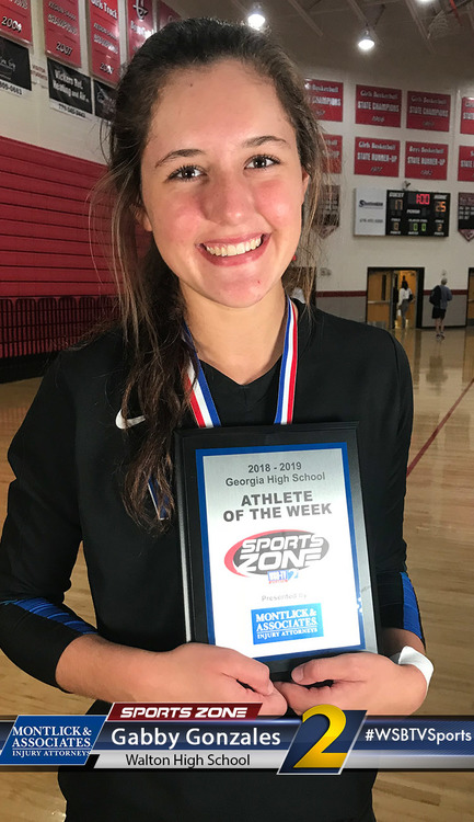 Smiling high school Athlete of the Week award recipient in gym, holding Sports Zone plaque and medal.
