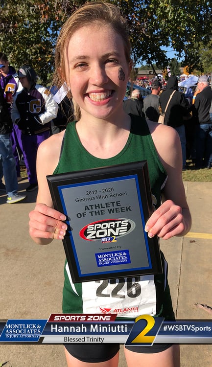 Smiling female athlete of the week holding award plaque, wearing jersey number 226, outside on sunny day.