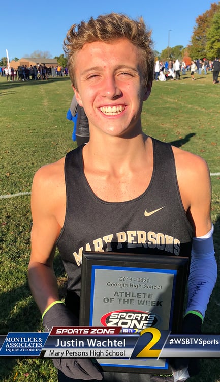 Smiling high school athlete of the week holding award, standing on sports field in sunlight
