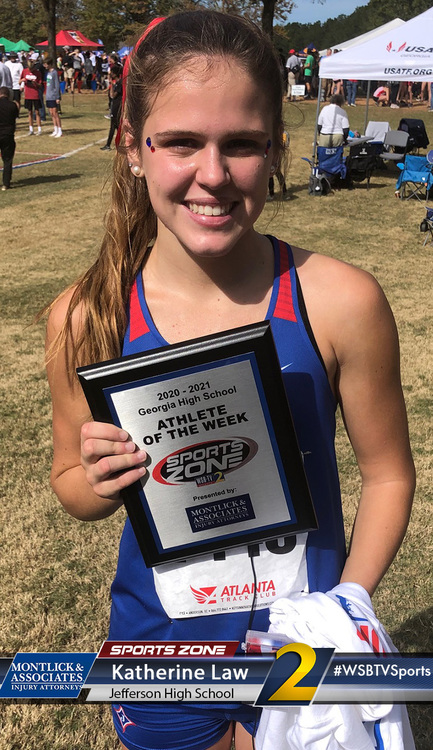 Young female athlete proudly holding "Athlete of the Week" award at sports event, smiling at camera.