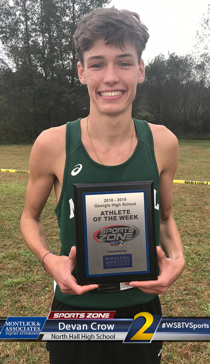 Young smiling male athlete holding 'Athlete of the Week' award plaque while standing on a sports field