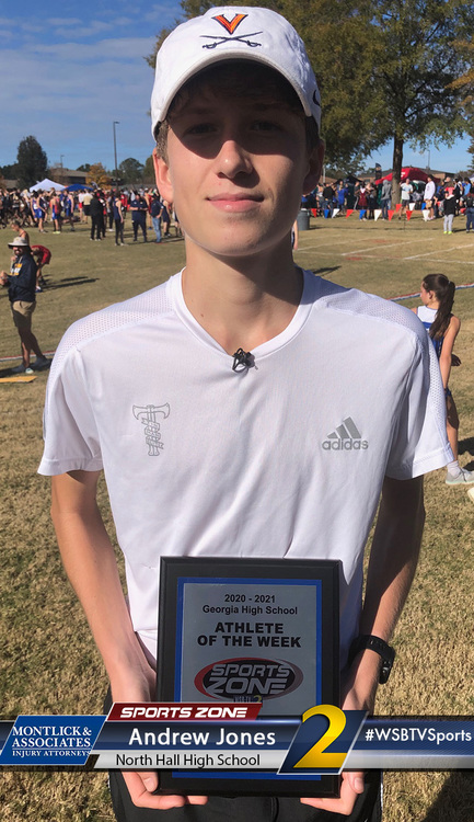 Young male athlete holding award plaque at high school sports event on sunny grass field.