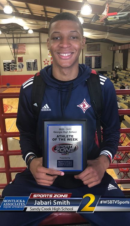 Smiling high school athlete holding Sports Zone Athlete of the Week award at school gym equipment room
