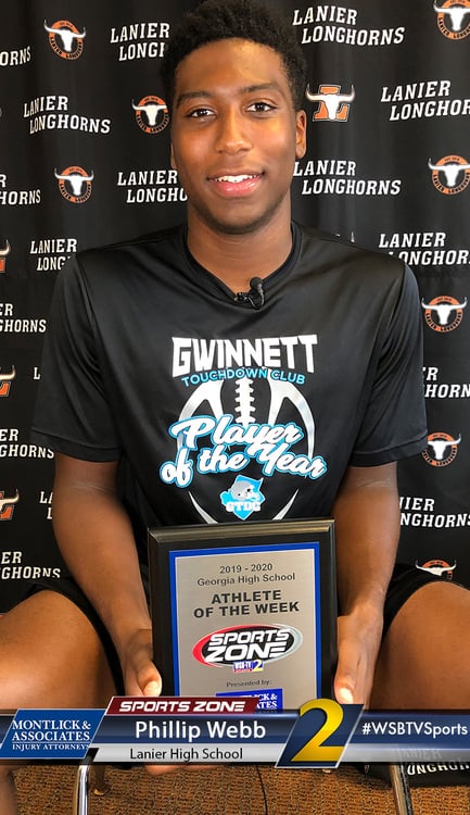 Lanier HS football player of the year wins award, smiling and holding plaque with school logo backdrop