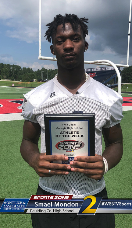 High school athlete named Athlete of the Week holds award plaque on football field at Georgia high school stadium.