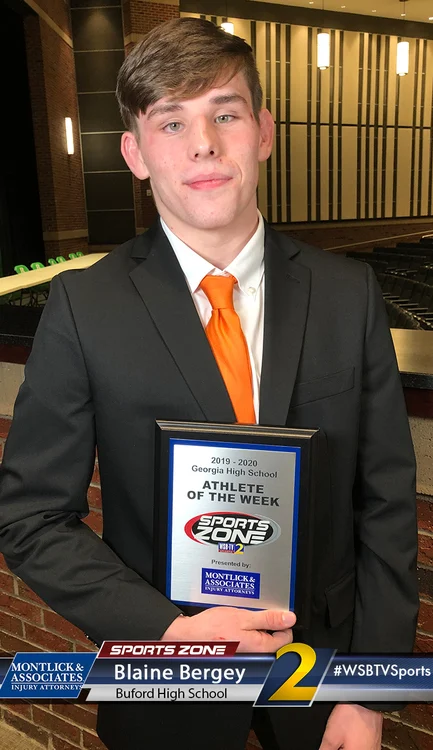 Young male student-athlete wearing suit and orange tie holding "Athlete of the Week" award plaque.