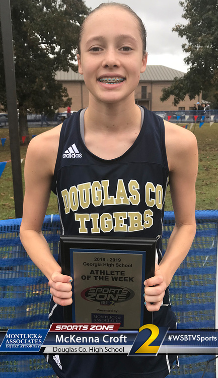 Young smiling female athlete holding "Athlete of the Week" award from Douglas County High School sports program.