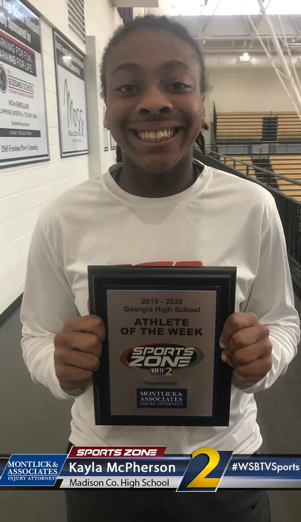 Smiling high school athlete holding "Athlete of the Week" award plaque for sports accomplishments.