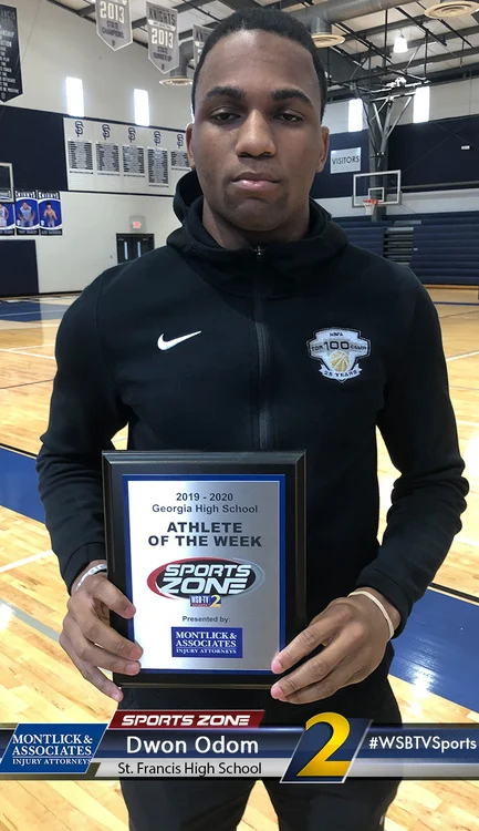 High school athlete of the week holds award plaque while standing on basketball court in gym uniform.