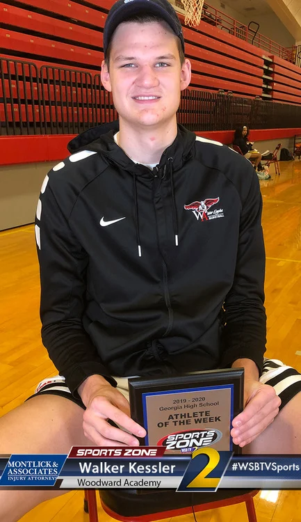 Smiling Woodward High School athlete holding Sports Zone Athlete of the Week award in a gymnasium.