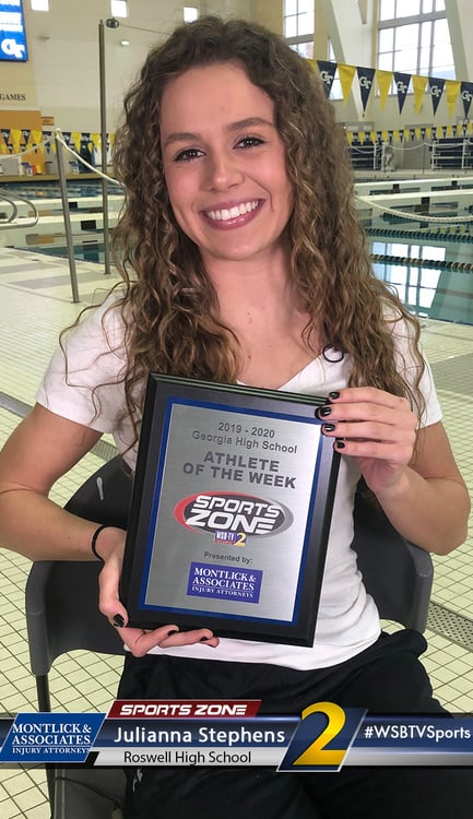 Smiling high school athlete holding Athlete of the Week award plaque at swimming pool, celebrating achievement