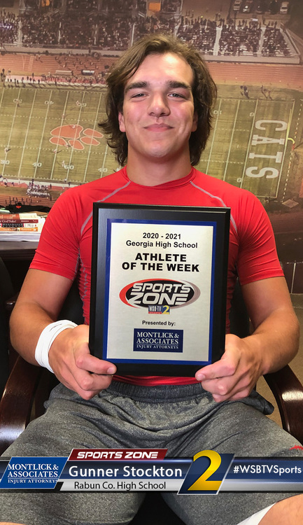 High school athlete of the week posed with award plaque at football stadium, smiling proudly