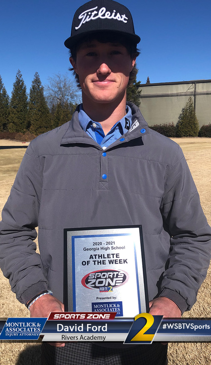 Student athlete of the week David Ford smiles while wearing a Titleist hat and holding his award plaque outdoors at a school sports field.