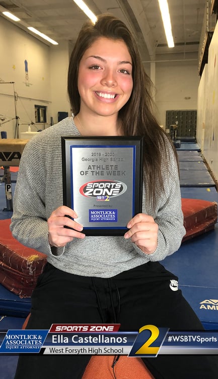 Smiling female student athlete of the week holds Sports Zone award plaque in gymnasium.