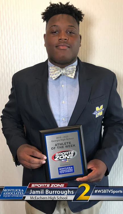 Smiling high school student in suit holding Athlete of the Week award from Sports Zone TV station.