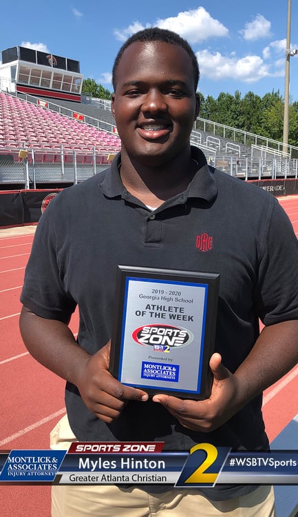 Sports Zone male athlete of the week holding award plaque on running track, smiling at camera
