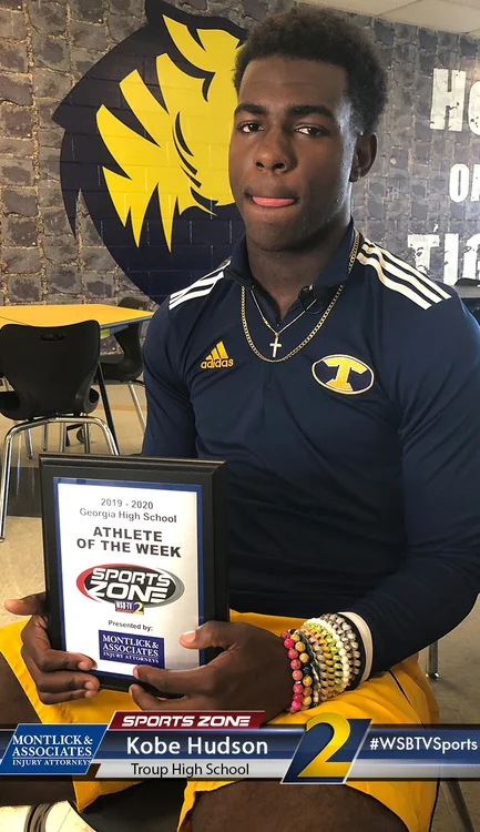 High school football player holding "Athlete of the Week" award from Sports Zone, a local sports news outlet.
