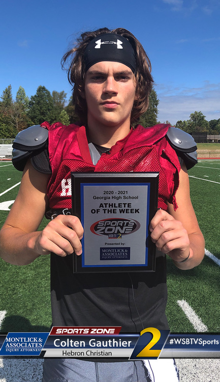 High school football player holding Athlete of the Week award on football field, wearing shoulder pads