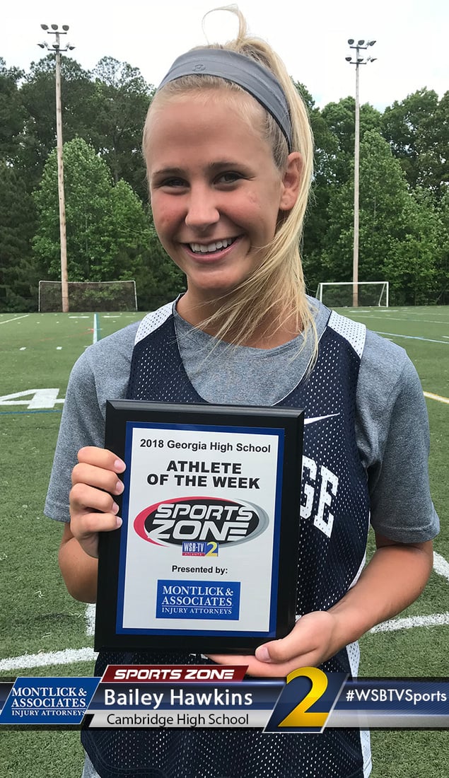 Smiling female high school athlete holding "Athlete of the Week" award on sports field
