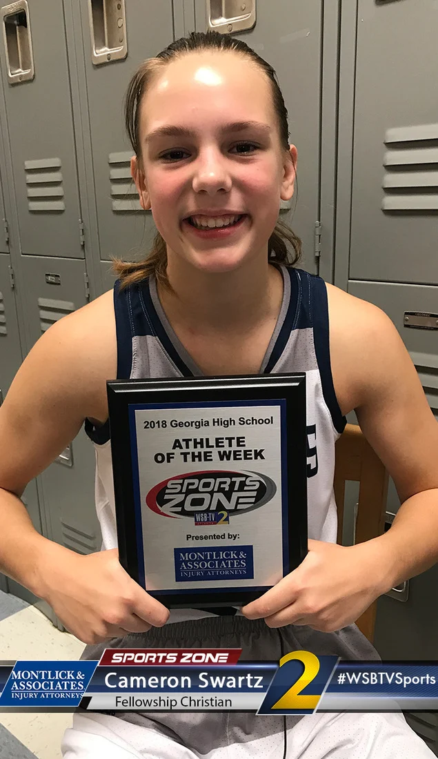 Young female athlete holding an "Athlete of the Week" award, smiling proudly in a school locker room.