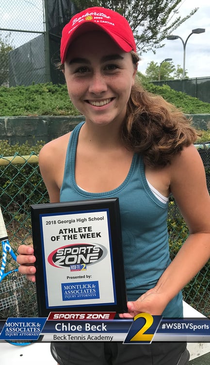 Young female athlete holding "Athlete of the Week" award, smiling in athletic top and red cap.