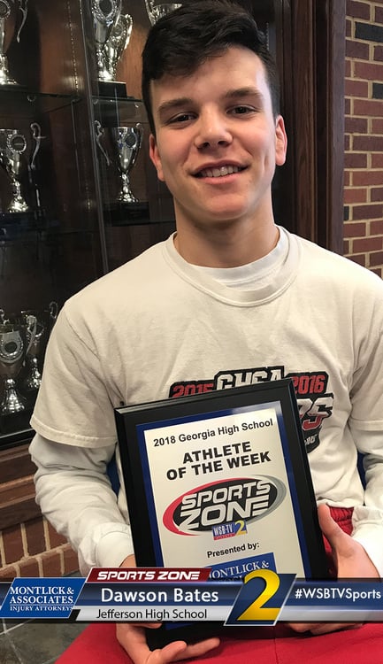 Smiling high school athlete of the week holding award plaque in sports-themed room.