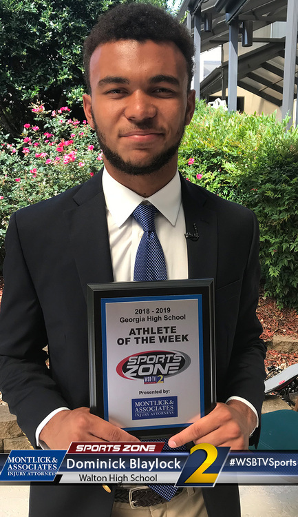 Smiling high school athlete of the week holding award plaque outside school building