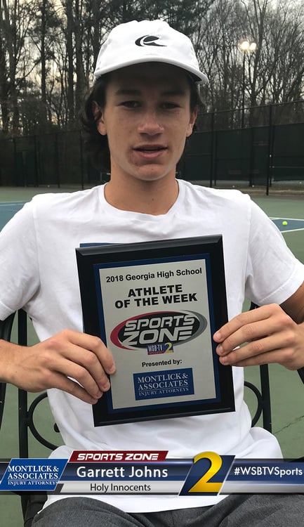 The image shows a young male athlete outdoors holding a plaque that says "2018 Georgia High School ATHLETE OF THE WEEK, Presented by MONTLICK & ASSOCIATES INJURY ATTORNEYS". He is wearing a white t-shirt with a Nike cap and logo. A possible alt text under 100 characters for an injury attorney website could be: High school Athlete of the Week award winner sponsored by Montlick & Associates Injury Attorneys This alt text concisely describes the relevant parts of the image while including keywords related to the sponsoring law firm to help with SEO. It avoids identifying the individual by name.