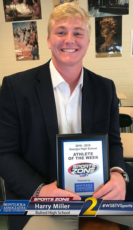 Smiling high school athlete of the week holding Sports Zone award plaque, wearing suit and white collared shirt.