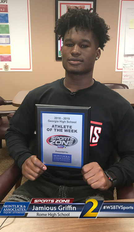 African American high school student athlete of the week holding award plaque, smiling in classroom
