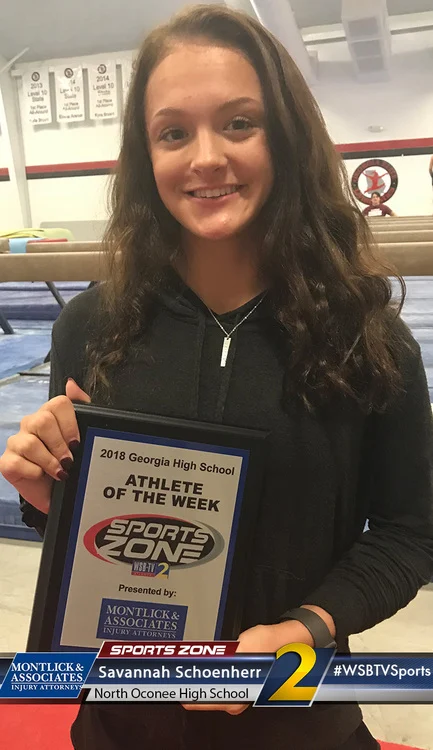Smiling high school athlete of the week holds award plaque in gymnasium setting.