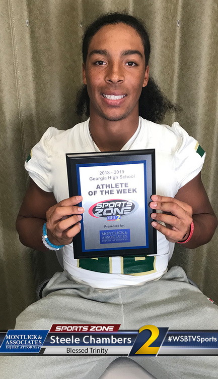 Smiling teen athlete of the week award winner holds plaque, wearing green and white sports uniform.