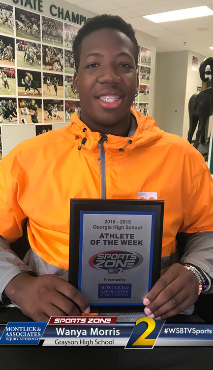 Smiling high school athlete of the week holding award plaque in orange windbreaker jacket.