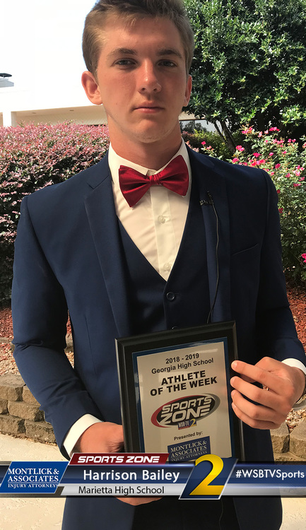 Teenage boy in suit holding Athlete of the Week award outside, smiling at camera. High school sports achievement.