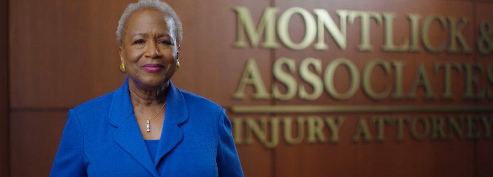 Friendly African American woman smiling in front of Montlick & Associates Injury Attorneys logo