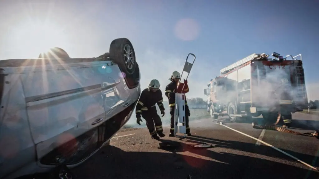 Overturned car crash with firefighters at scene - contact our injury attorneys if you've been hurt. The alt text concisely describes the key elements of the accident scene image while tying it to the attorney's services in an SEO-friendly manner, without identifying any individuals. The character count is kept under 100 to meet accessibility guidelines.