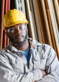 Serious construction worker in hard hat amid wooden planks, considering workplace injury claim